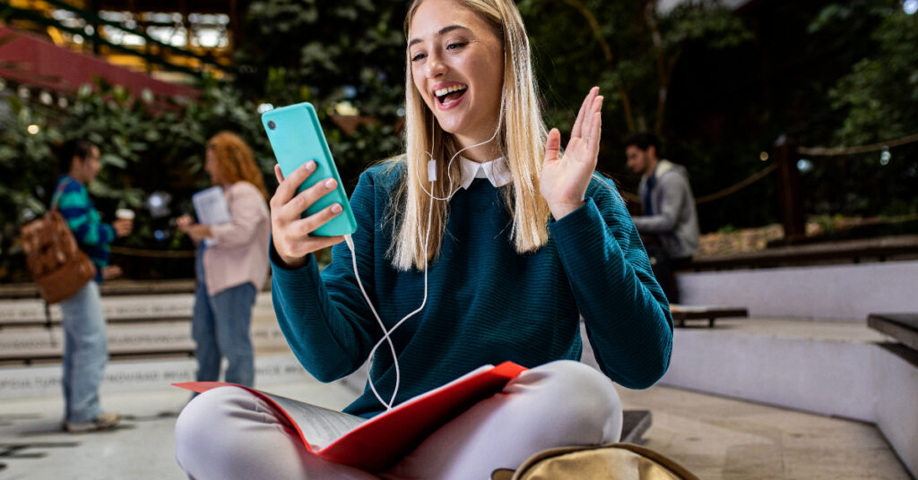Portrait of female student siting in campus using smartphone for video call.