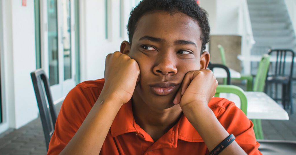 Teenage Black boy with hands under chin looking to the side, annoyed