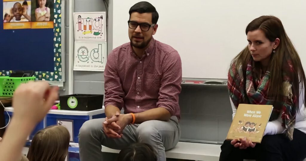 White male and female teachers teaching from the front of a classroom, in front of a whiteboard