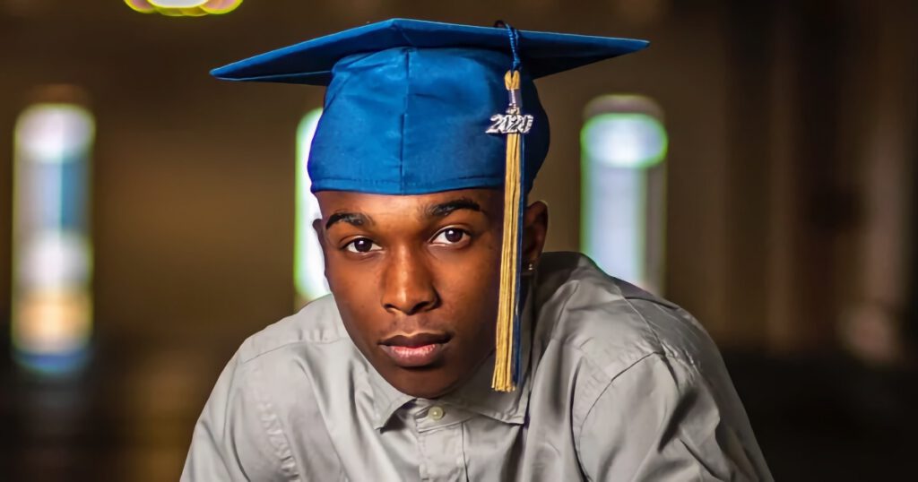 Young Black man wearing a blue graduation cap looking at the camera.