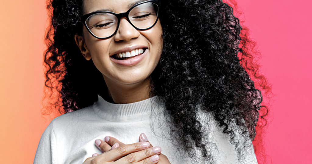 Young Black woman smiling with eyes closed and hands on her heart
