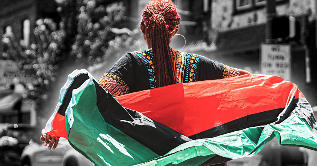 Black woman with braids dancing in the street, wearing African clothing and wrapped in an African flag.