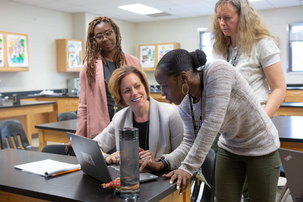 Four teachers gathered around a laptop talking to each other.