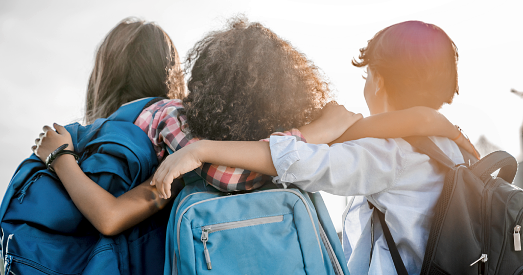 Three school-aged children with their arms around each other.