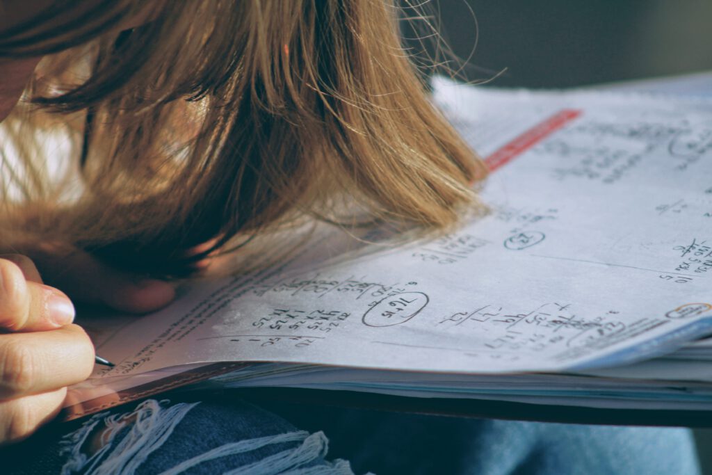 a student off camera leaning over a notebook doing math equations
