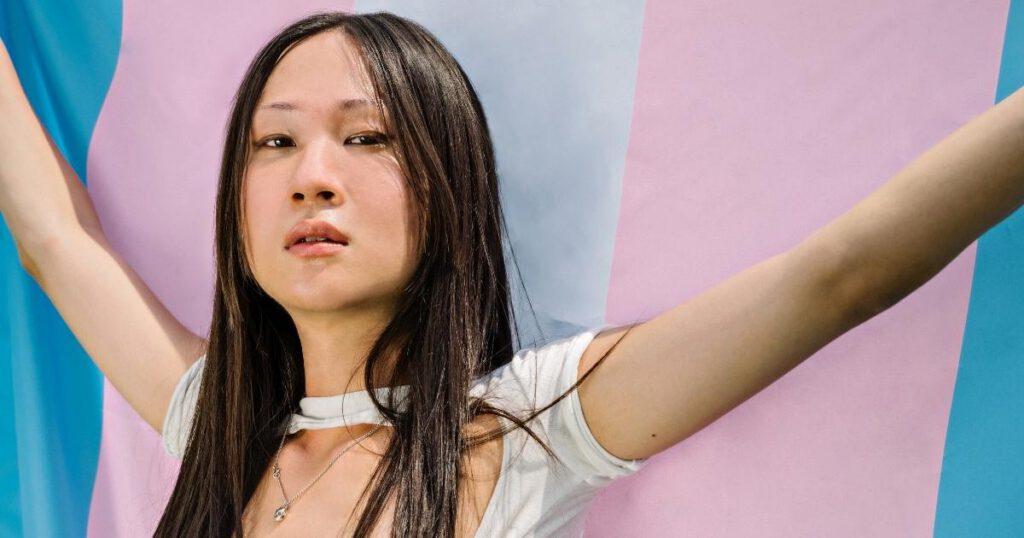 Asian teenage girl standing in front of a transgender flag