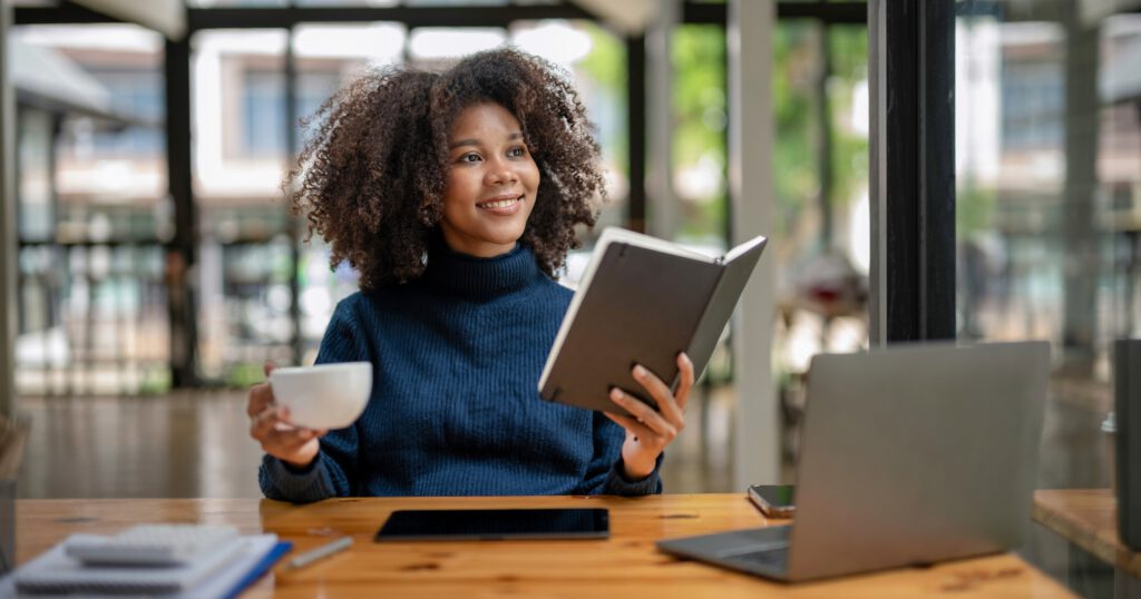 Young Black woman smiling with coffee and reading a book