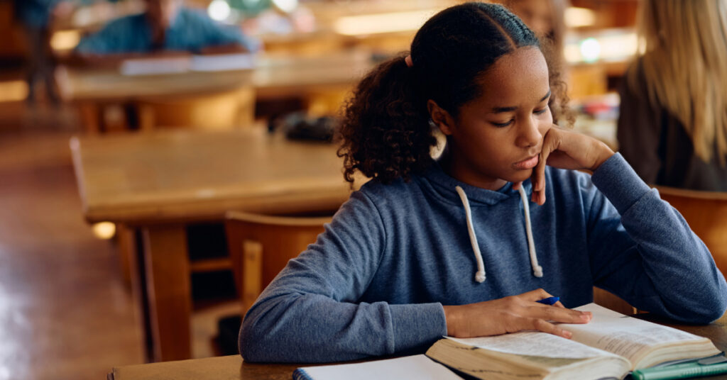 African American teenager girl studying from a book during a class at high school.