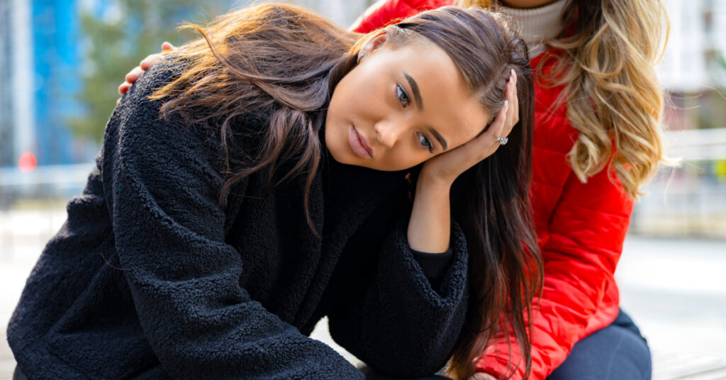 Friend consoling young unhappy and sad woman while sitting in city. Teen problems