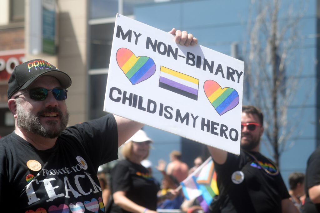 A sign at a rally that says "my non-binary child is my hero"