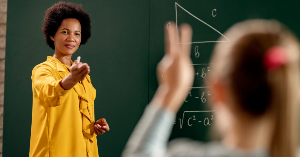 African American teacher asking a question and aiming at elementary student in the classroom.