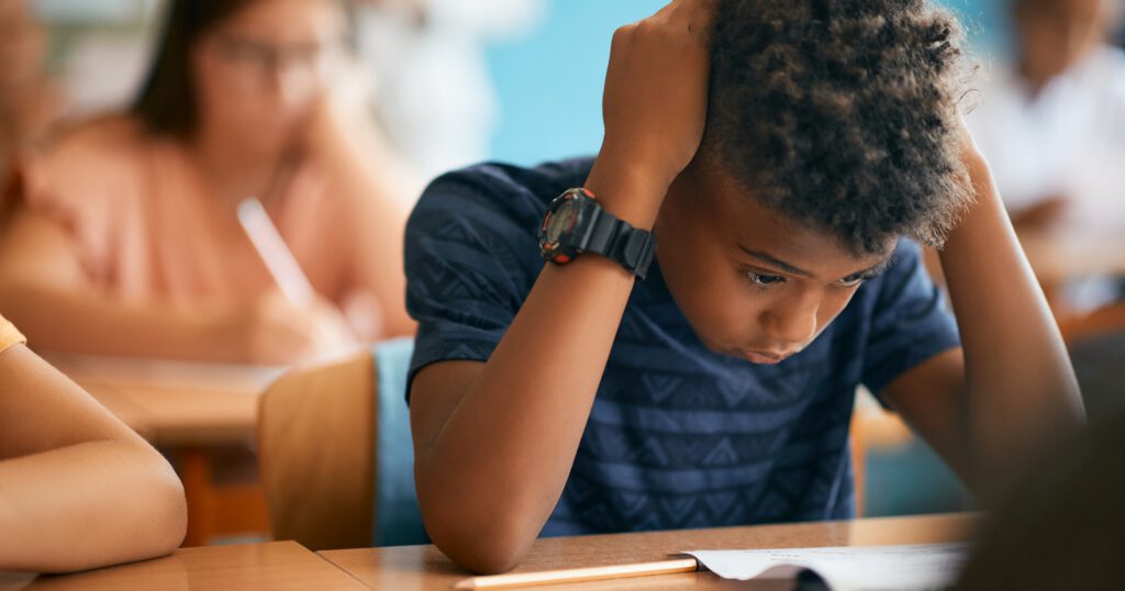 Uncertain African American schoolboy having exam during a class in the classroom.