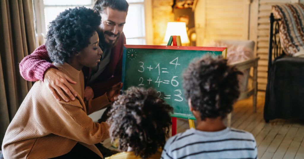 Happy black children learning maths with parents at home.