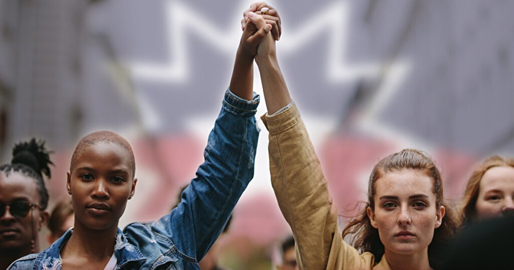 Black young woman and white young woman, holding hands in solidarity at a protest or rally