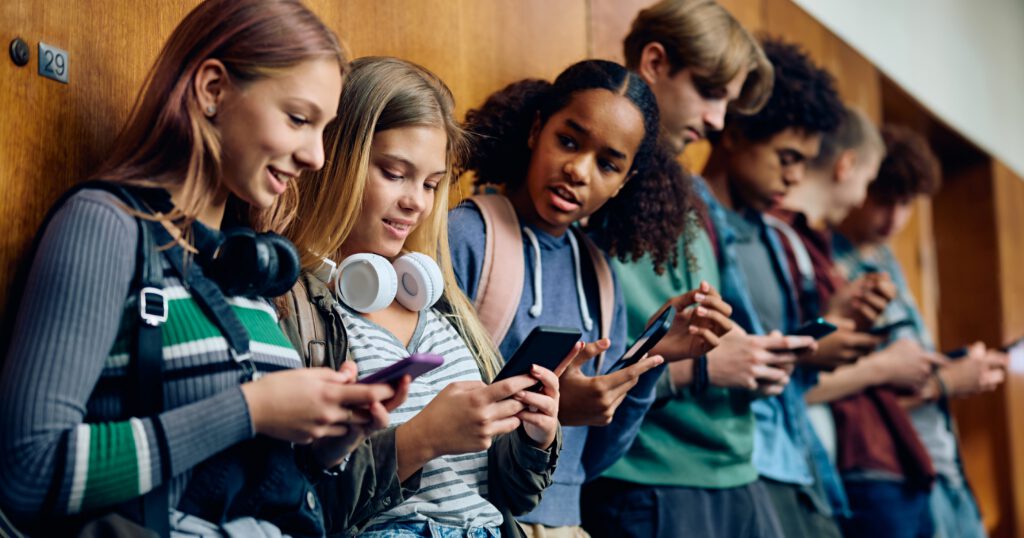 Multiracial group of high school students using their cell phones in hallway.