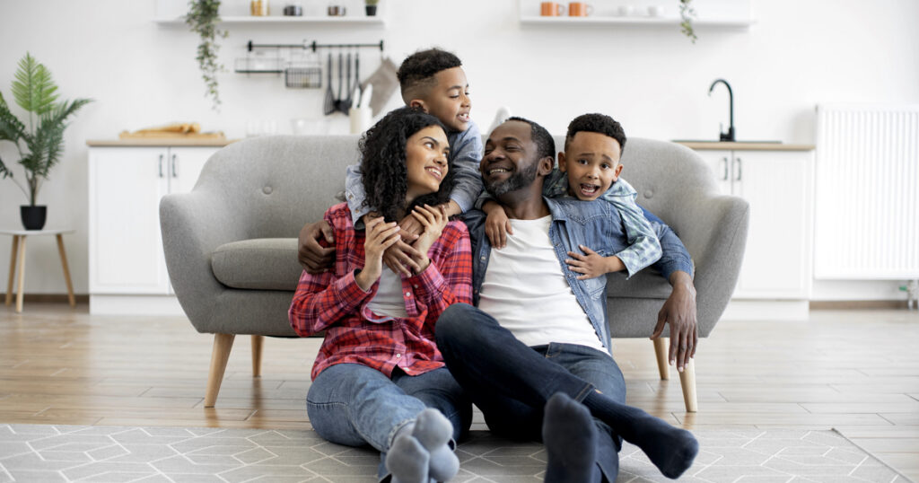 Energetic multiethnic children in jeans clothes talking to relaxed adults while staying indoors on sunny day.