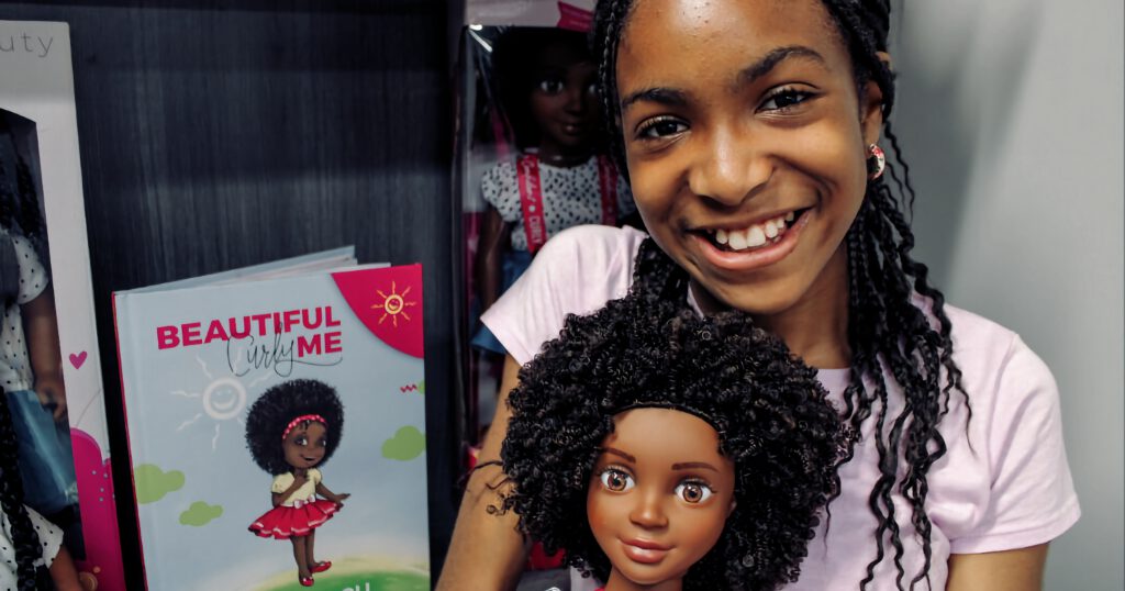 Zoe Oli holding a Beautiful Curly Me Doll, with a Beautiful Curly Me Book in the background
