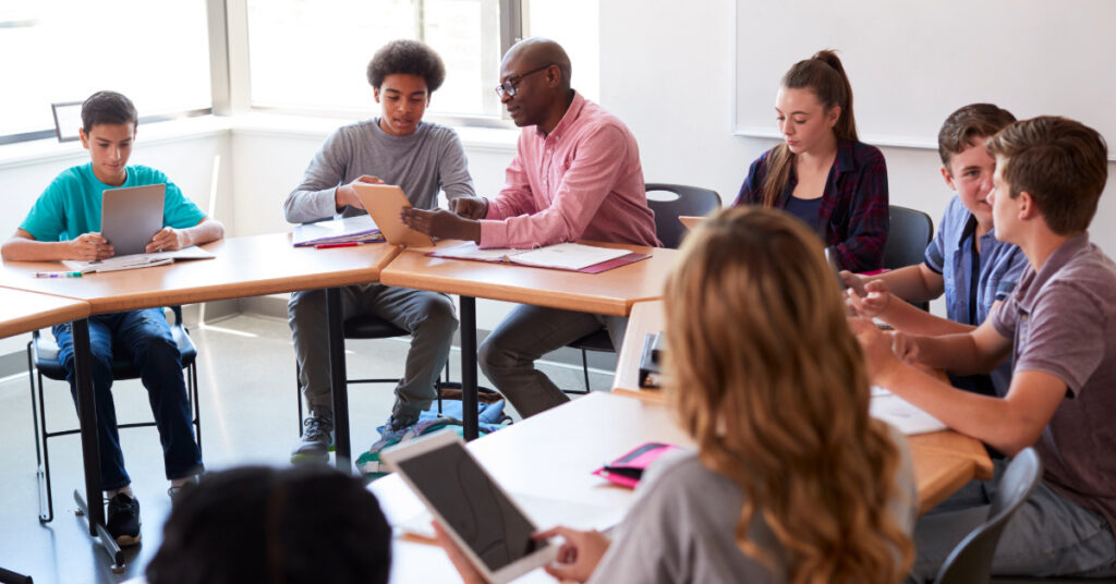 High School Teacher With Pupils Using Digital Tablets In Technology Class