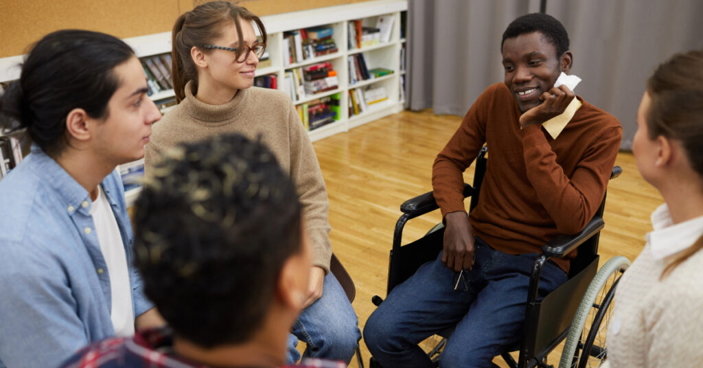 Multi-ethnic group of people sitting in circle, focus on handicapped African man sitting in wheelchair