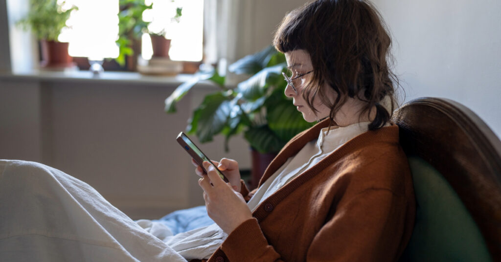 girl with eyeglasses lying resting on bed, using phone, scrolling through social network