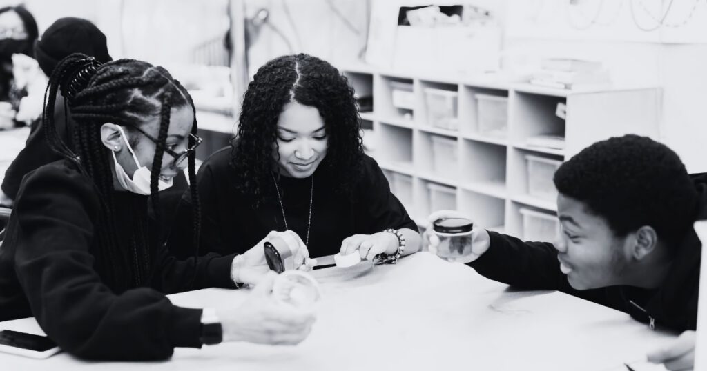 Black and white image of a Black woman teacher working in a classroom with two Black students