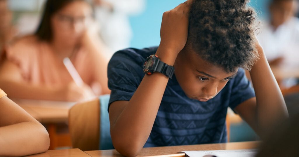 Uncertain African American schoolboy having exam during a class in the classroom.