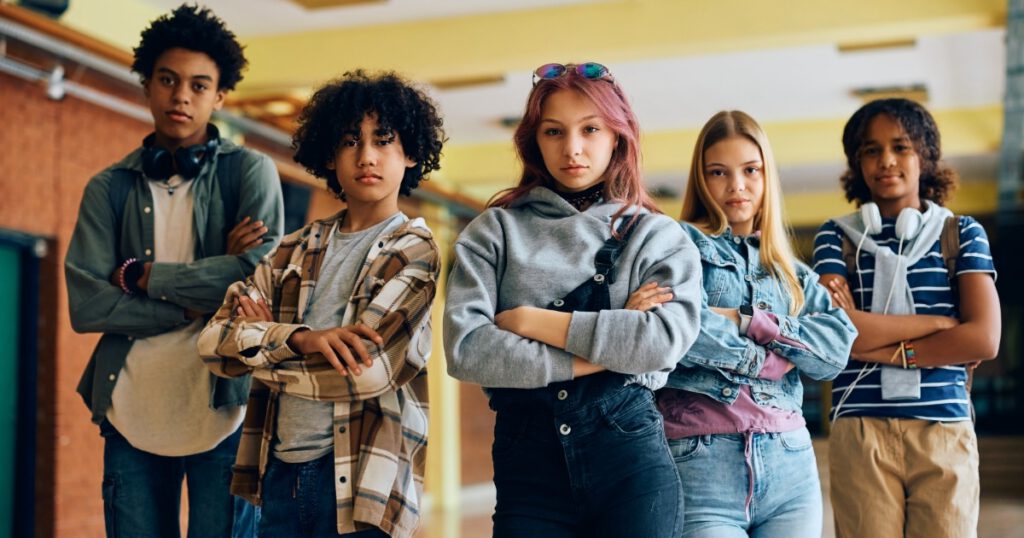 Young, diverse students standing in a school hallway with arms crossed.