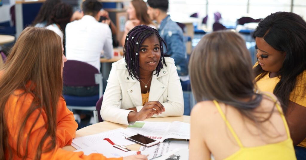 Female higher education students discussing project in college classroom