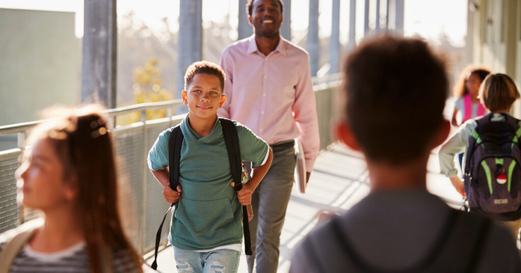 Male teacher and pupils walking on busy school campus
