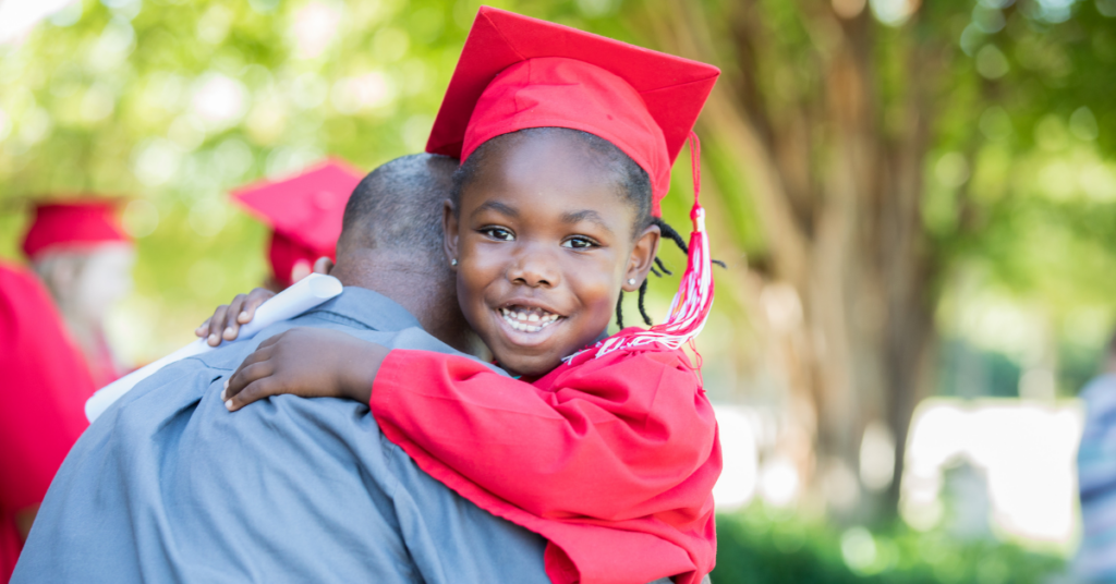 Young Black girl embracing her father at her kindergarten graduation ceremony