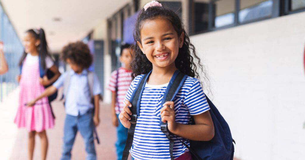 Latino and biracial students at school; Latina young girl smiling at the camera and wearing a backpack