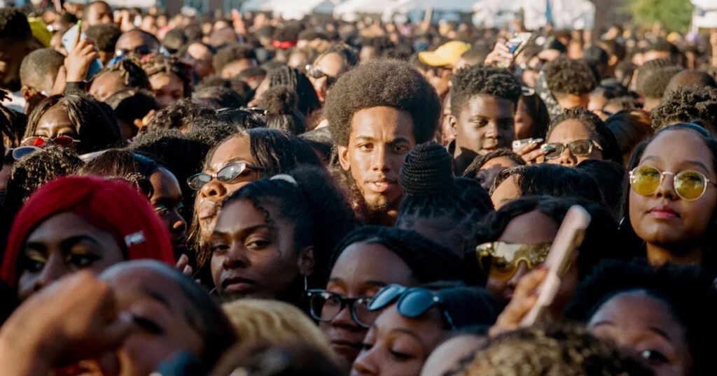 A crowd of young Black people at an event, protest, or demonstration; One young Black man looks at the camera with a serious expression