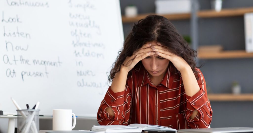 Teacher sitting at her desk problem solving with her hands on her head
