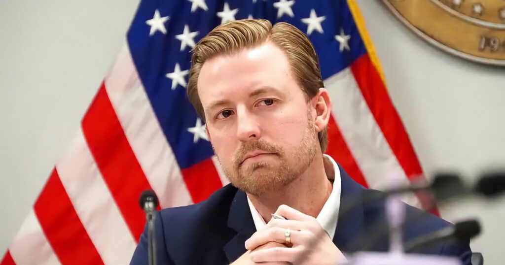 Ryan Walters State Superintendent of Education in Oklahama sitting at a desk in front of an American Flag