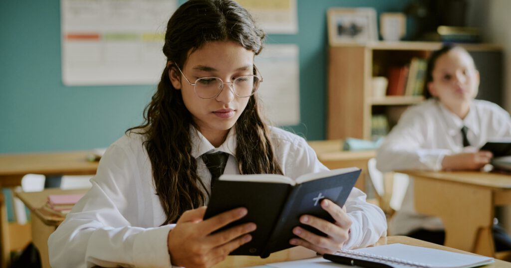 Female student of color reading the Bible in a school classroom