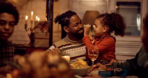 Happy Black father and daughter having fun during Thanksgiving lunch at dining table.